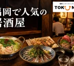 福岡の居酒屋で、もつ鍋、焼き鳥、刺身、ごまさば、日本酒が並ぶ夜の食卓を描いたアイキャッチ画像