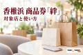 イオンモール香椎浜の商品券「絆」の利用案内を紹介する、商業施設を想起させる架空の空間の買い物袋とスマートフォンのイメージ