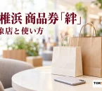 イオンモール香椎浜の商品券「絆」の利用案内を紹介する、商業施設を想起させる架空の空間の買い物袋とスマートフォンのイメージ