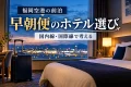 旅行かばんを置いた架空のホテル客室と夜明けの空を描いた、福岡空港の早朝便に備える前泊の紹介用イメージ