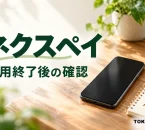 ネクスペイの利用終了後の確認を案内する、机の上のスマートフォンとメモ帳のイメージ。公式アプリ画面ではありません。